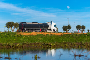 Wall Mural - Heat-insulated tanker truck with dangerous goods labels parked next to a river and under the full moon.