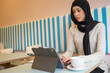 © Cultura Creative - Young woman in hijab using tablet in cafe