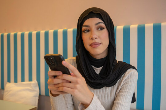 Young woman in hijab using phone in cafe