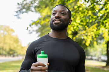 Wall Mural - Portrait of smiling athlete man holding water bottle after workout in park