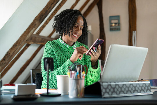 Smiling businesswoman using smart phone by desk in office