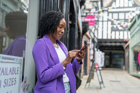 Smiling woman using smart phone while standing by building