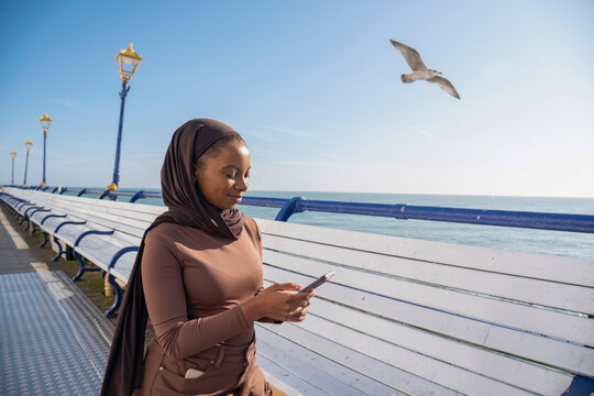 Muslim woman using smart phone while standing on pier on sunny day