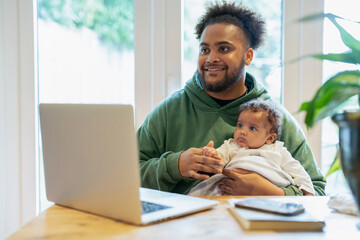 Wall Mural - Father holding baby daughter in front of laptop at home