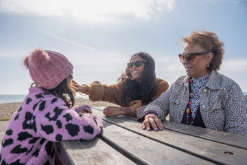 Poster - Grandmother, mother and daughter resting by picnic table on beach