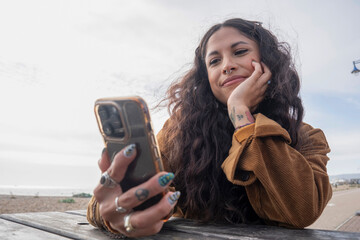 Poster - Smiling woman using smart phone while sitting by picnic table on beach