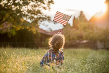 Wall Mural - Cute little patriot sitting on the meadow and holding the national flag of United States