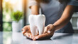 Woman's hands shield large white 3D tooth on white table, symbolizing dental care, protection, and health