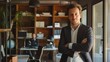 © Togrul - Confident businessman standing in his office with arms crossed. There is a bookshelf and a man working in the background.