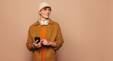 Fototapeta Panele - Cheerful man using smartphone with vibrant peach background