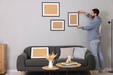 Wall Mural - Man hanging picture frame on gray wall at home