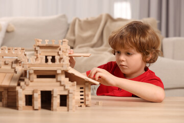 Sticker - Cute little boy playing with wooden castle at table in room. Child's toy