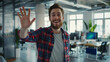 Portrait of smiling young man waving hand while standing in creative office