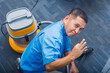 © Mdv Edwards - A friendly middle-aged janitor in a blue uniform making the ok sign confirming that the vacuum cleaner works. Employed at an office building.