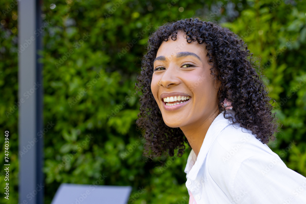 Young biracial woman with curly black hair smiles brightly outdoors at ...