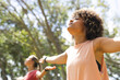 © Wavebreak Media - Young biracial woman with curly hair enjoys a moment of relaxation outdoors, arms outstretched, with