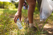 © Wavebreak Media - Person picks up a plastic bottle from the grass, holding a clear trash bag and collecting trash