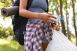 © Wavebreak Media - A young biracial woman holds a water bottle and a plastic bag, collecting trash during a hike