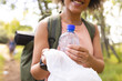 © Wavebreak Media - Young biracial woman with curly hair smiles while holding a plastic bottle and a bag outdoors, colle