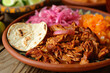 A plate of cochinita pibil, a traditional Mexican dish made with slow-roasted pork, achiote paste, and orange juice, often served with tortillas.