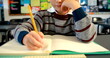 A Caucasian child is focused on writing in a notebook at a school desk