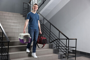 Sticker - Travel with pet. Man holding carrier with cute cat and bag on stairs indoors