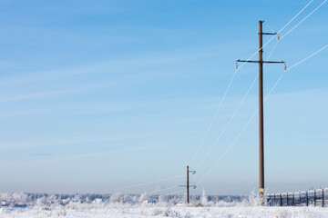 electric high-voltage pylons in the winter landscape with snow-covered trees , clear cold morning