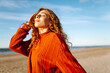 © maxbelchenko - Portrait of a beautiful curly woman on the beach in cold sunny weather. Spring time.Travel, weekend, relax and lifestyle concept.
