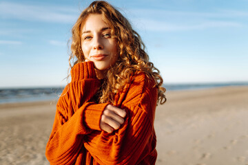 Portrait of a beautiful curly woman on the beach in cold sunny weather. Spring time.Travel, weekend, relax and lifestyle concept.