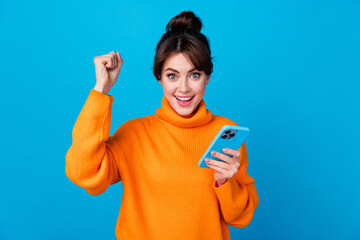 Wall Mural - Photo of good mood lucky woman dressed orange sweater rising fist winning game modern gadget isolated blue color background