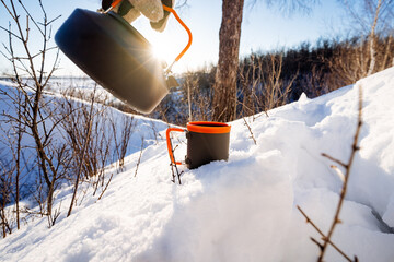 Wall Mural - kettle against the background of the glare of the sun, camping equipment, utensils on a winter hike, cup for tea, pour a hot drink into a mug, camping in the forest.