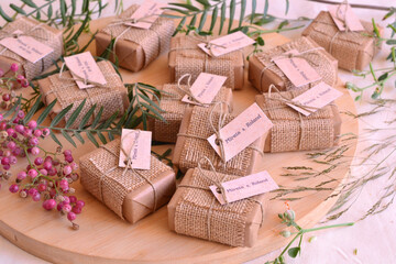 Autumn fall wedding decoration guest gifts rustic style soaps wrapped in brown craft paper jute fabric ribbon and custom labels with names, wodden table background with red berries and green leaves