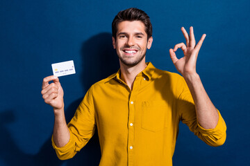 Poster - Photo portrait of attractive young man hold credit card show okey dressed stylish yellow clothes isolated on dark blue color background