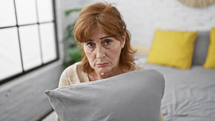 Canvas Print - Distressed middle aged woman in bedroom, a solemn expression of stress, worry and sadness as she sits on bed, hugging pillow, crying in anger and depression