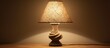 A table lamp with a burlap shade is positioned on a table, casting a shadow on a plain wall. The lamp emits light creating a contrast between light and shadow.