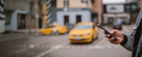 A man calls a taxi in the city through an app on his phone. Close-up. Yellow car on the background.