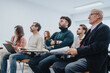 © qunica.com - A varied group of attentive people participate in a corporate training session. They are sitting in a bright, contemporary office space, focused on the presenter.