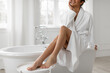 © Home-stock - Smooth female legs after depilation routine, black lady sitting on bathtub in bathroom at home, free space Body care concept