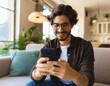 © jesp 0505 on insta - Smiling young male using mobile phone app playing game online at home, sitting on comfortable sofa