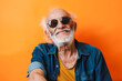Front view of a happy senior man posing with optimism and sunglasses over colorful orange background