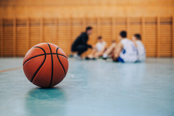 Wall Mural - A basketball on court with junior team in blurry background.