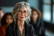 © Margo_Alexa - A mature woman with glasses and curly gray hair attentively listening in a meeting.