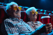  An elderly couple watches a movie in a cinema wearing glasses - a refreshing take on active aging. Copy space.