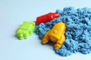 Poster - Bright kinetic sand and plastic toys on light blue background, space for text