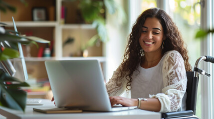 happy latina woman sitting at desk in wheelchair working on laptop