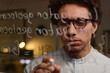 © AnnaStills - Closeup of young man wearing eyeglasses developing computer code writing it on glass wall