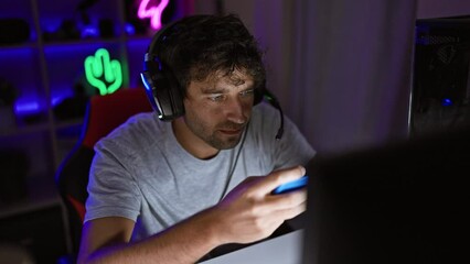 Canvas Print - A handsome man with a beard and headphones engages with a smartphone in a neon-lit gaming room at night.