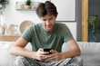 © Pixel-Shot - Young male soldier with mobile phone sitting on sofa at home