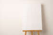 A blank white canvas is displayed on a wooden easel, with copy space