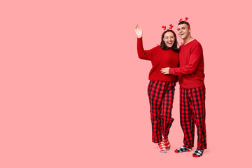 Sticker - Happy young couple in Christmas pajamas on pink background